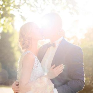 bride and groom kissing near a tree, leaves blurred above and behind them with the bright sun behind them. 